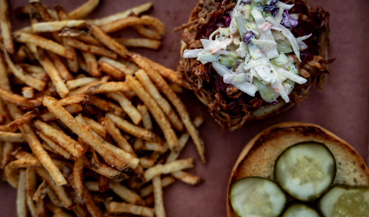 Fries and sandwiches with coleslaw and pickles on a plate, featuring the photographer's name.